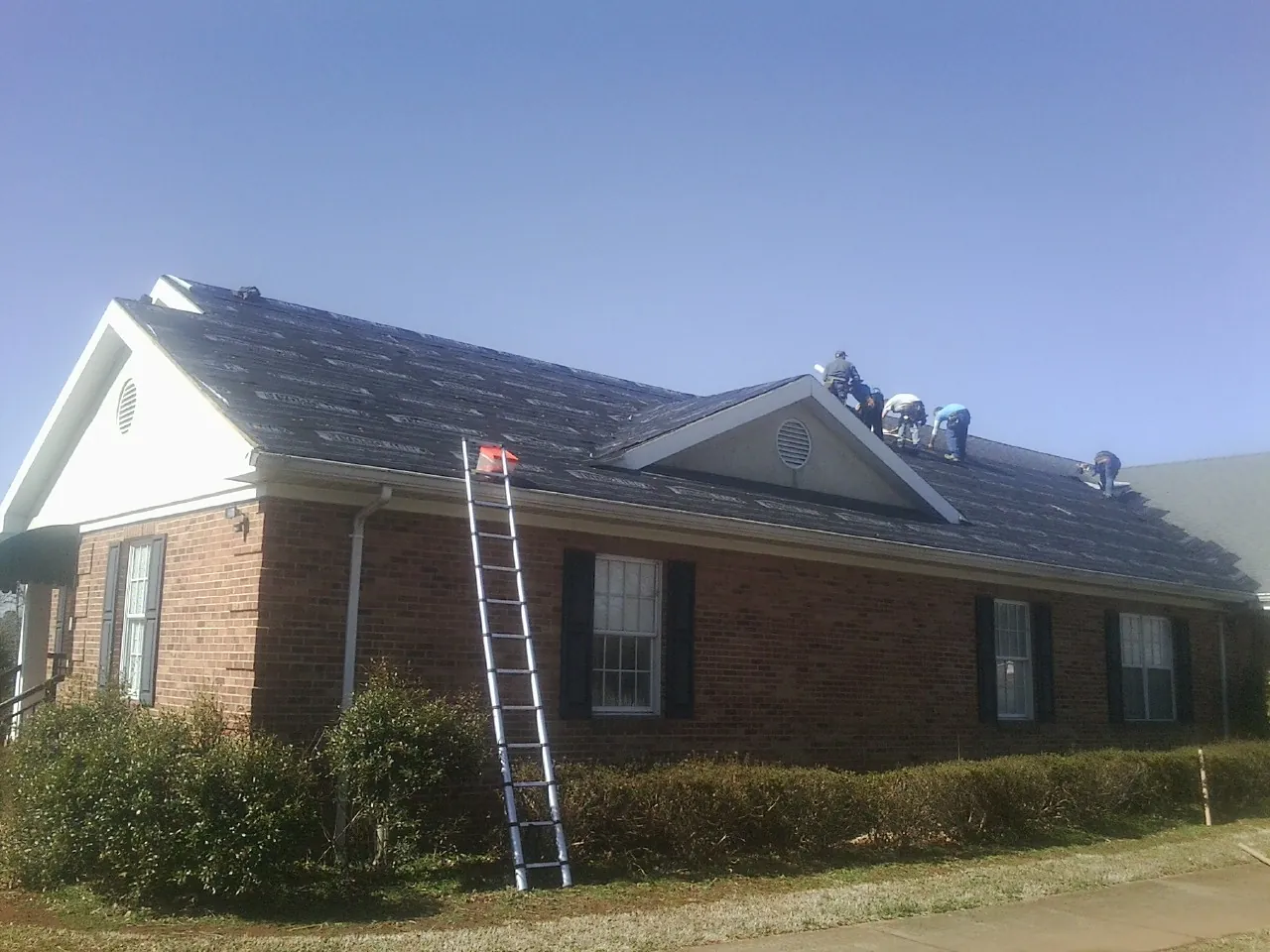 Crew tearing shingles off a brick ranch roof with a ladder set — Metal Roof Repair work by our crew in De Soto