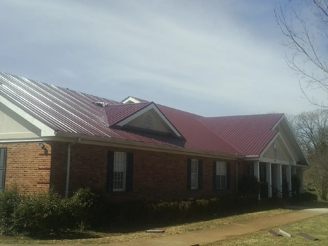Red metal roof with gabled entries on a long brick building, from a Hail Damage Roof Repair job in De Soto